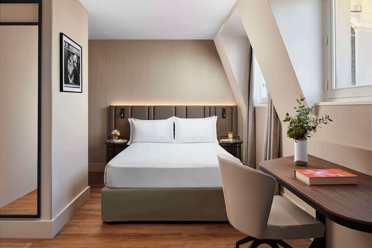 Een moderne hotelkamer met een bed, nachtkastjes, een bureau, een stoel en een raam.