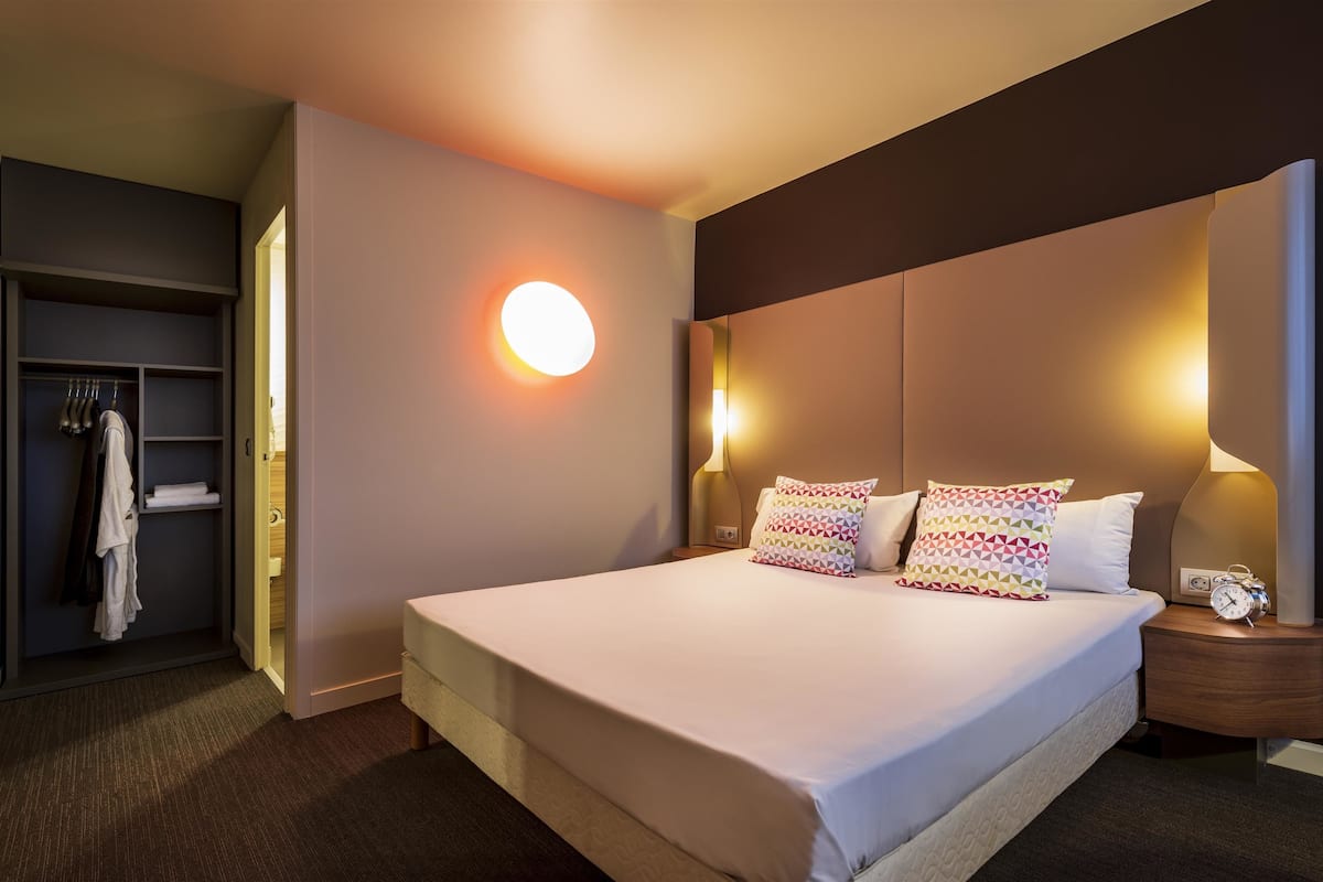 Ein Hotelzimmer mit einem großen Bett, Nachttischlampen, einem Nachttisch, einem Kleiderschrank und einer runden Wandleuchte.