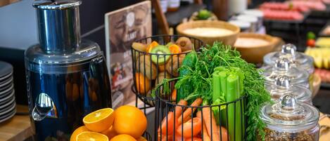 A buffet table with various food items including oranges, tomatoes, carrots, and celery. There are also containers of granola and a water dispenser.