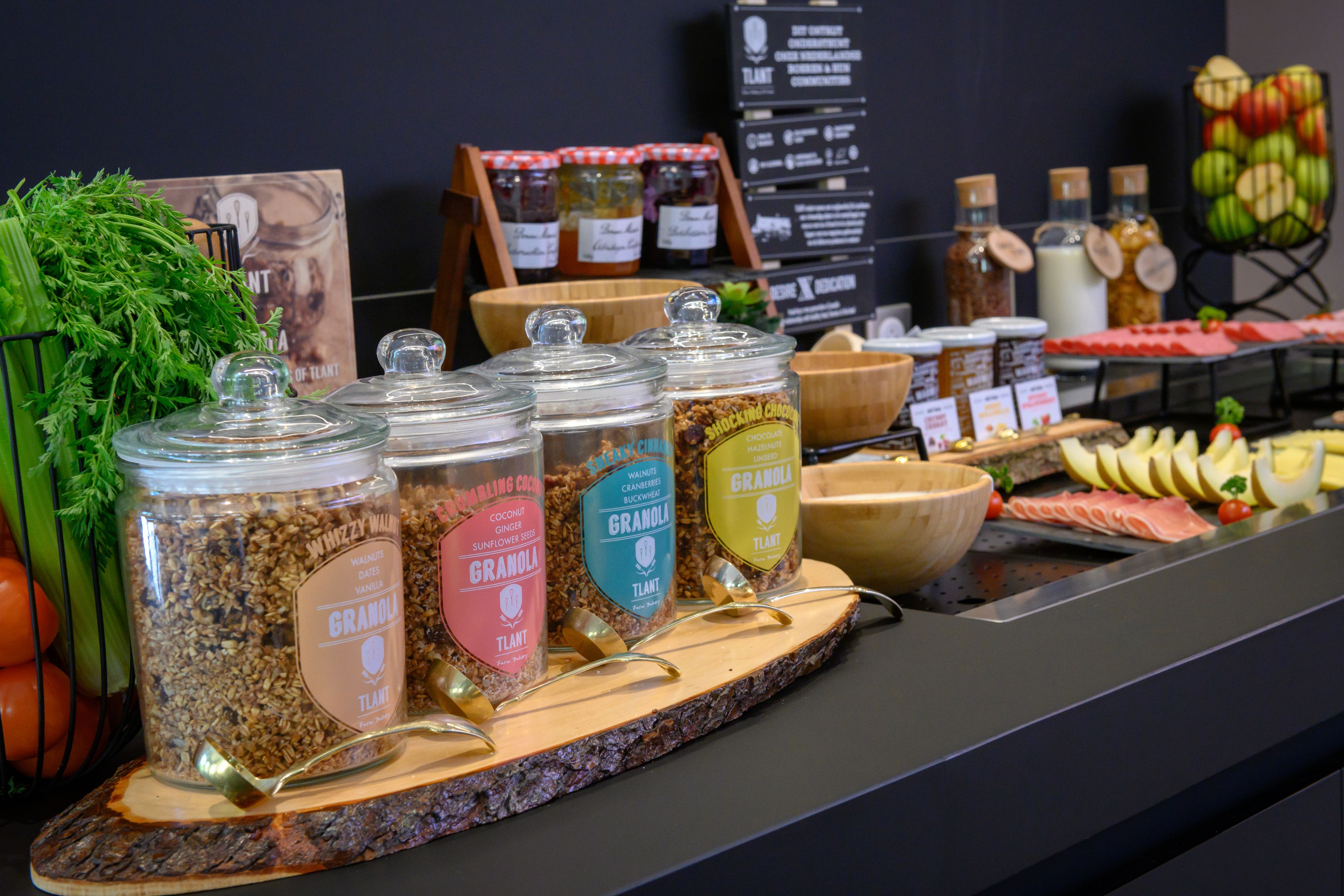 Una exhibición de diversas barras de granola y cereales, con etiquetas, una tabla de madera y una selección de frutas y verduras frescas.