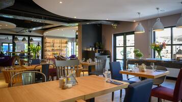 A modern restaurant interior with wooden tables, metal chairs, and pendant lighting.
