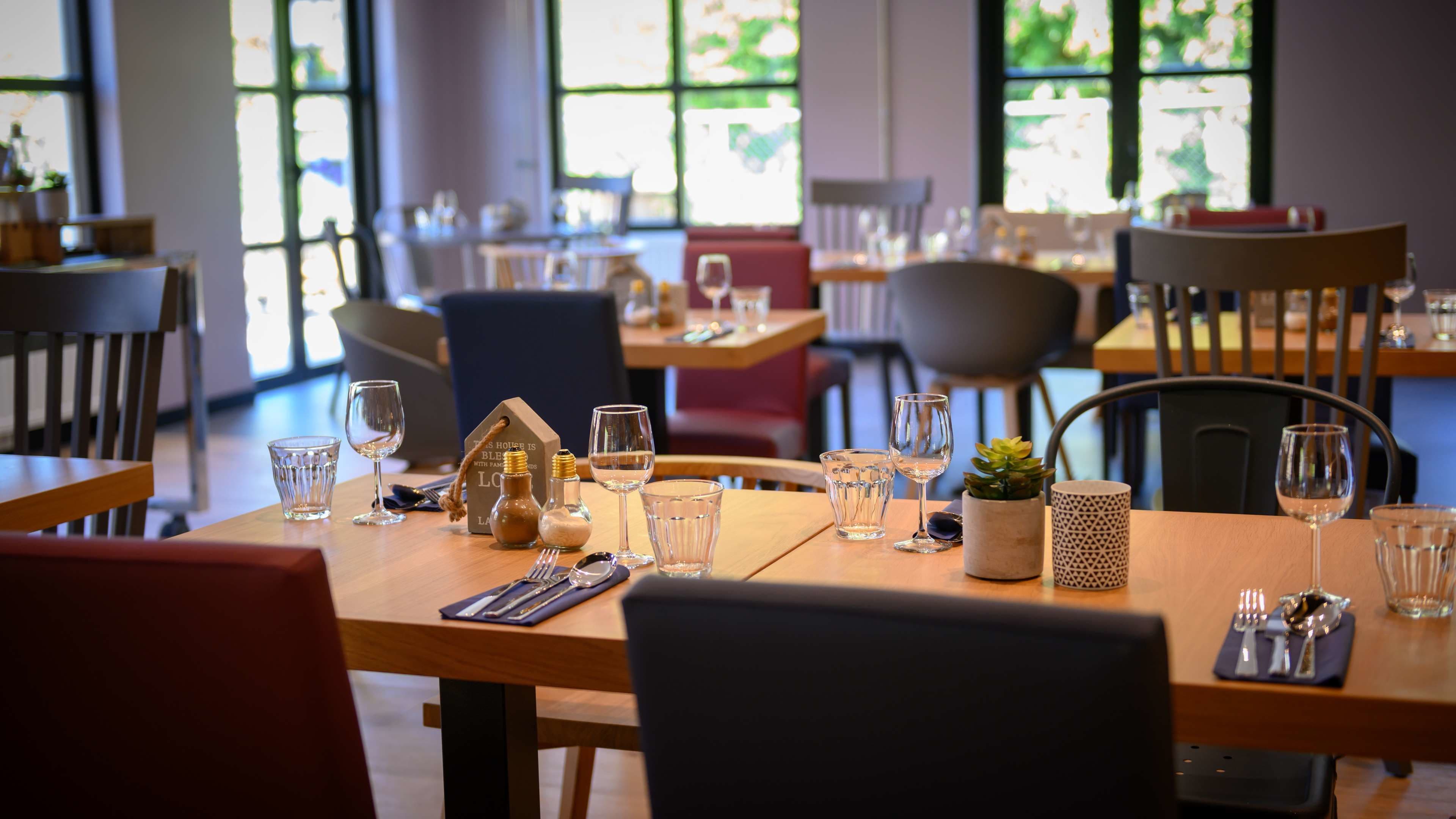 A restaurant with tables set for dining, clear glassware, and a small plant on the table.