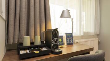 Een bureau in een hotelkamer met een lamp, een zwarte speaker, een brochure en een lade met spullen.