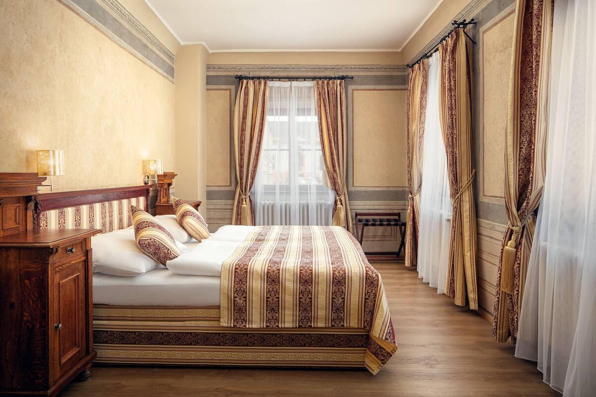 Habitación de hotel con una cama grande, cabecero de madera y cortinas.