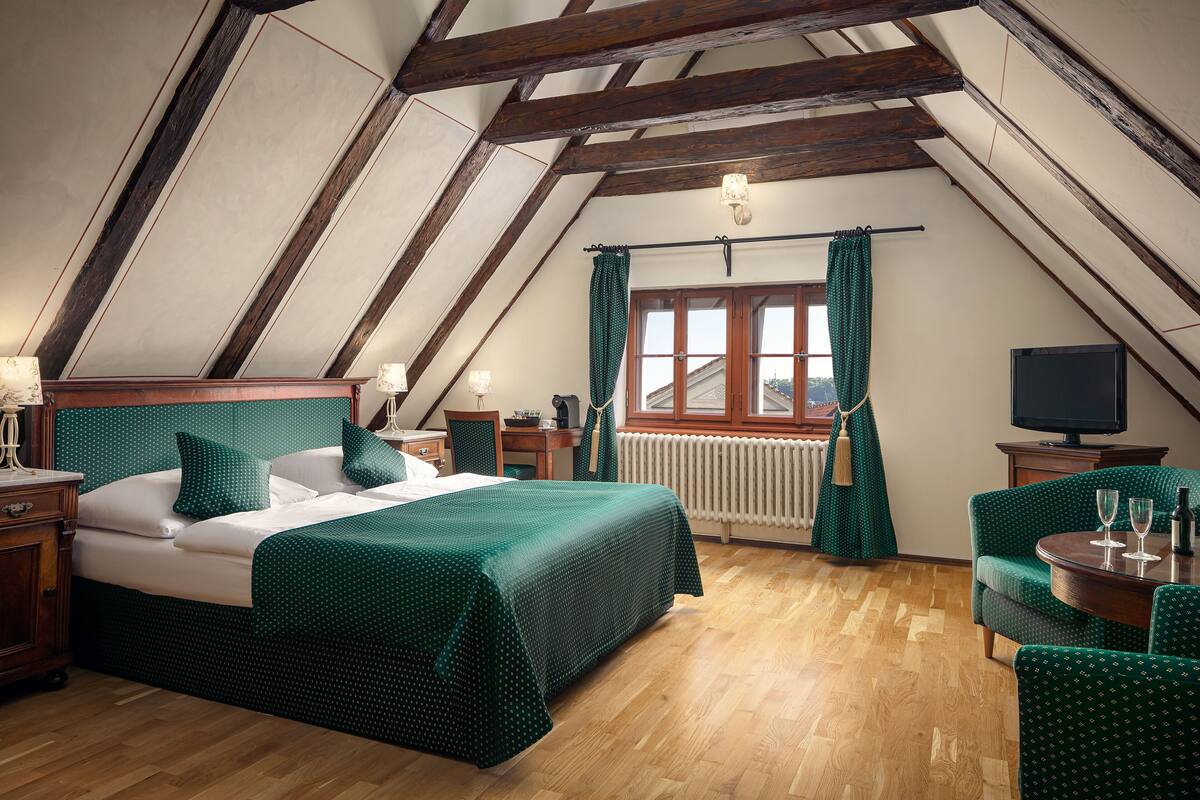Un dormitorio con una cama grande, televisión, una silla y ventana con cortinas.