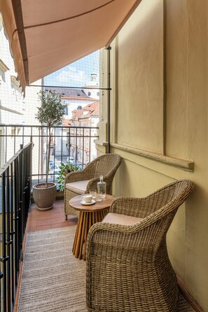 A balcony with wicker furniture, a potted plant, and a view of buildings. - The Charles (Prague)