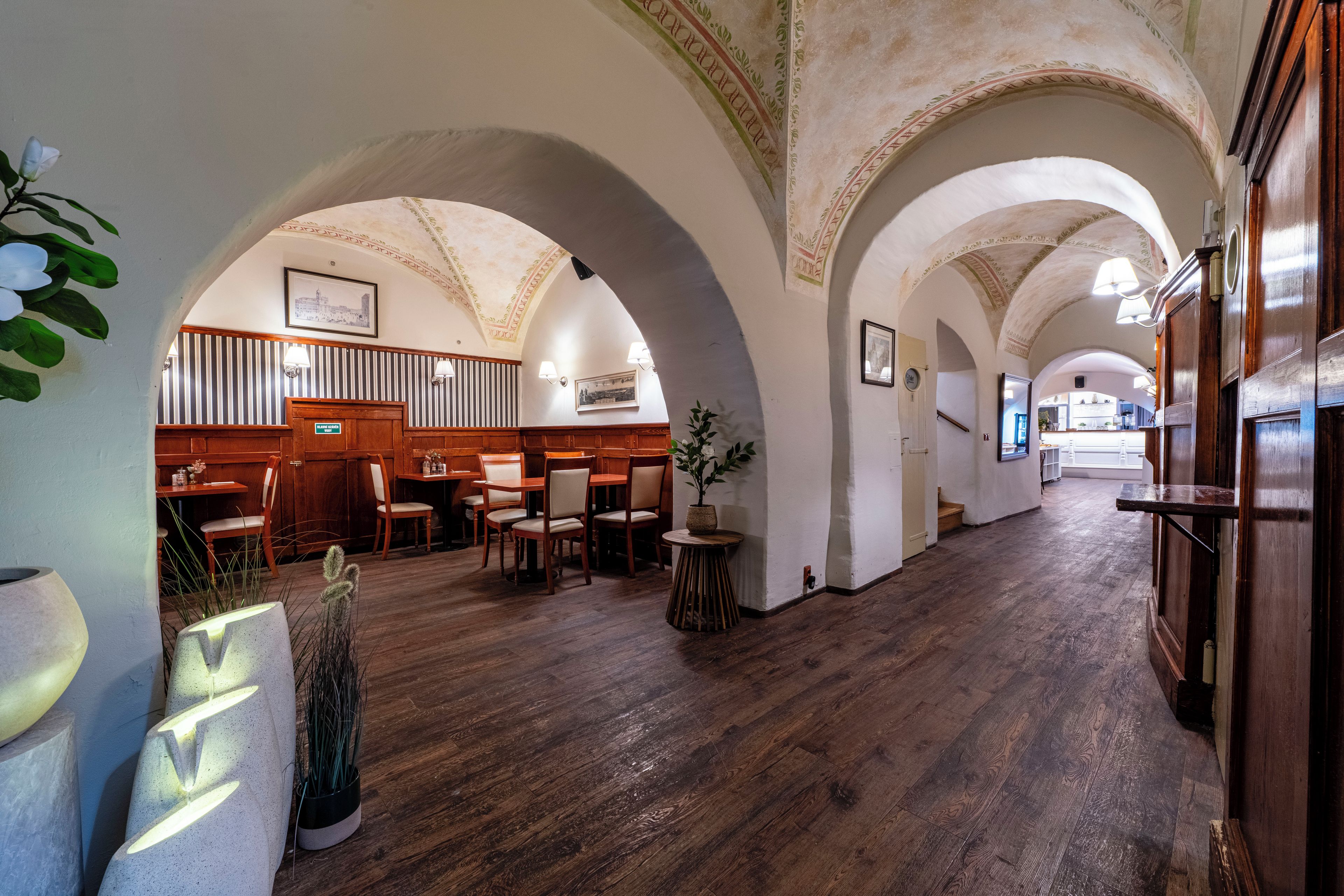 A hotel lobby with wooden flooring, arched ceilings, and a seating area with tables and chairs.