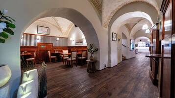 A hotel lobby with wooden flooring, arched ceilings, and a seating area with tables and chairs.