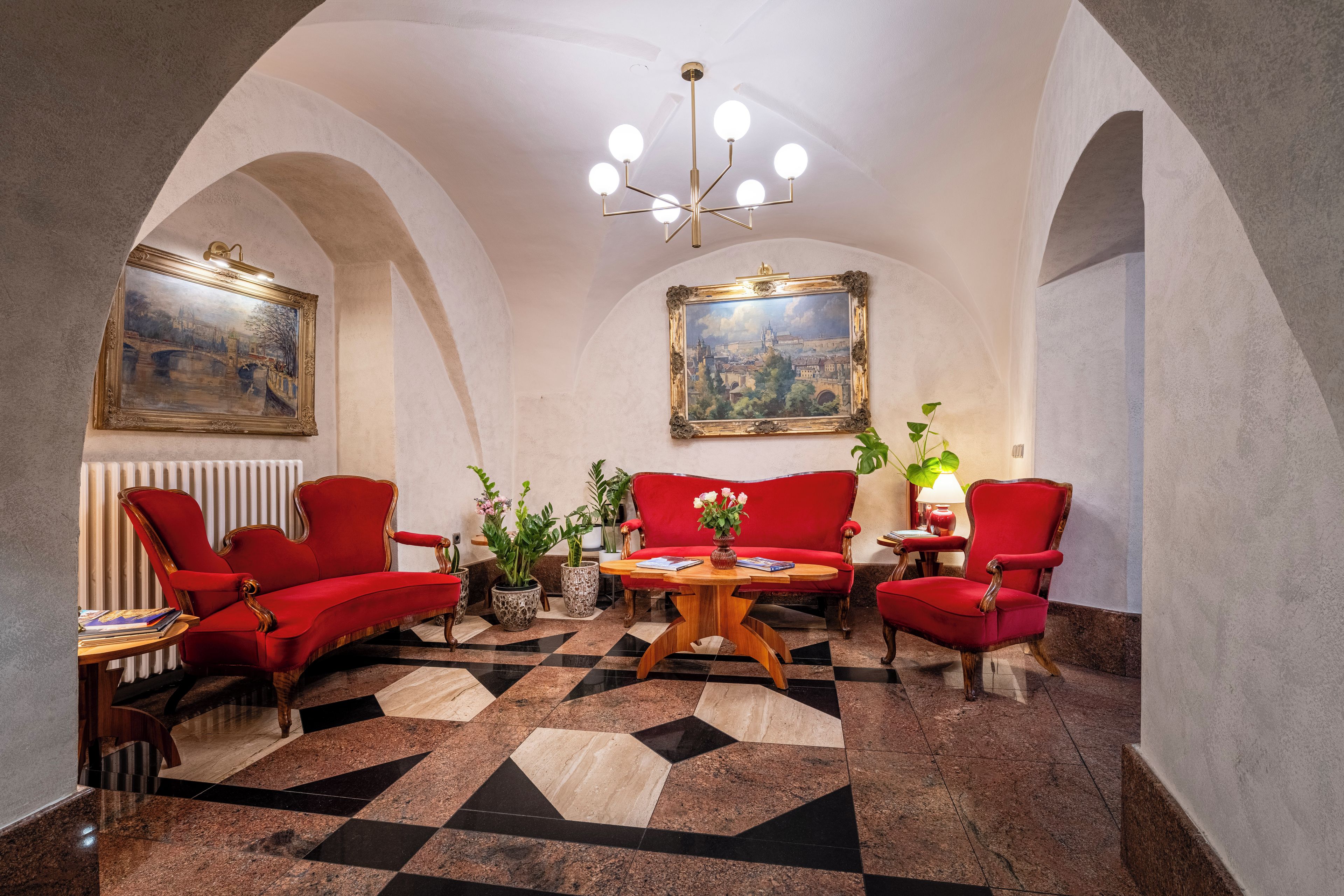 A room with a checkered floor, red upholstered chairs, a wooden coffee table, and two paintings on the walls.