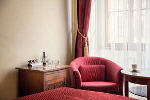 Une chambre d’hôtel avec une commode en bois, une chaise à pois rouges, une petite table et une fenêtre ornée de rideaux légers.
