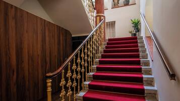 A grand staircase with red carpeted steps, ornate golden railings, and a wooden wall on one side.