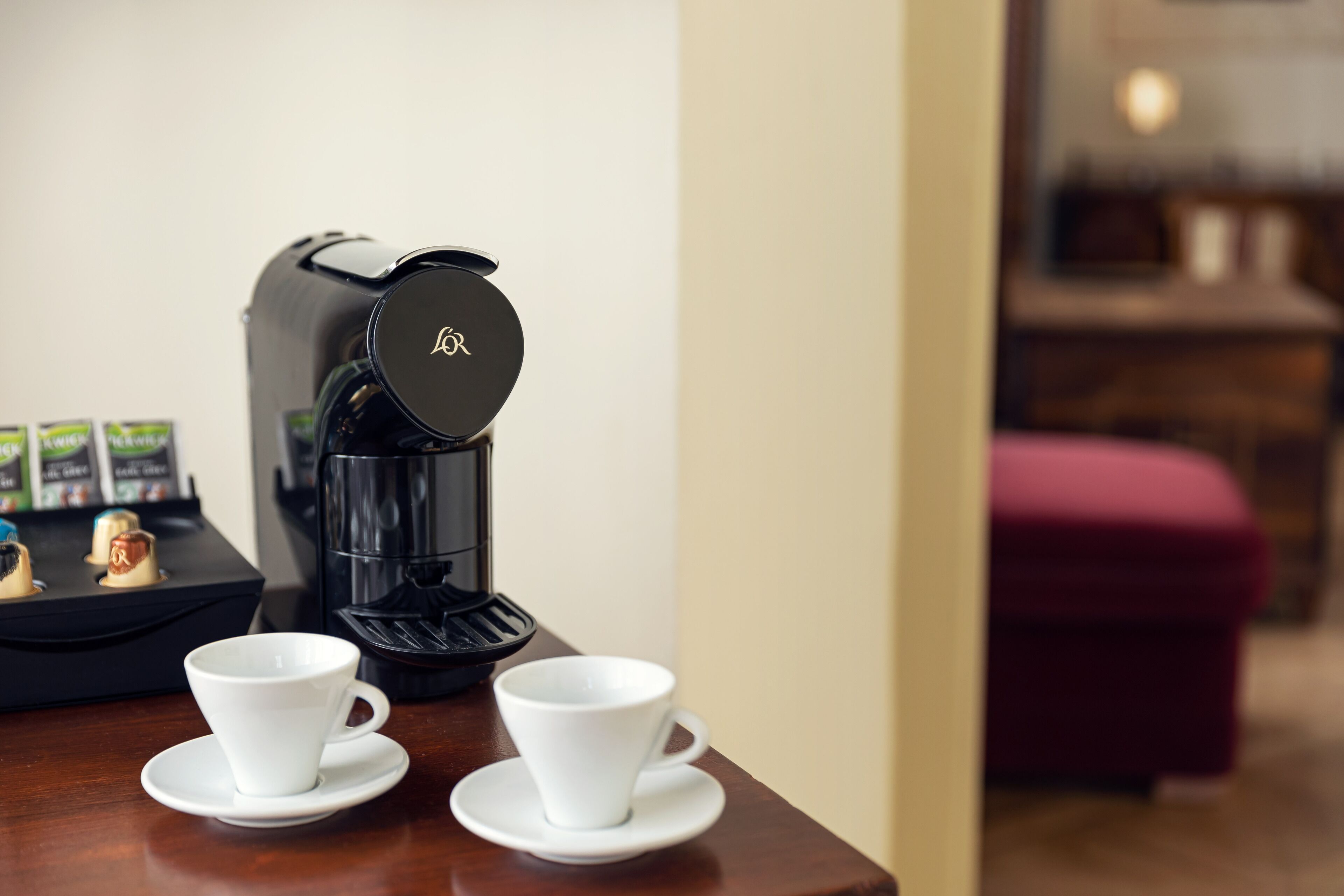 A coffee maker with two white cups on a wooden table.