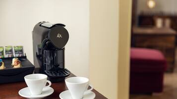 A coffee maker with two white cups on a wooden table.