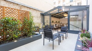 Un patio moderno al aire libre con mobiliario y cerramiento de vidrio.