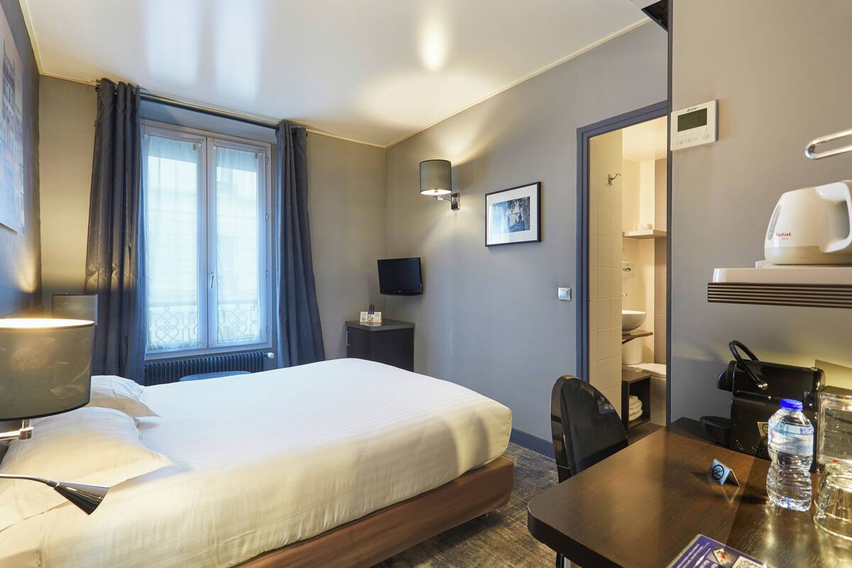 Une chambre d’hôtel équipée d’un lit, d’un bureau, d’une chaise, d’une télévision, d’une bouteille d’eau et d’une machine à café.