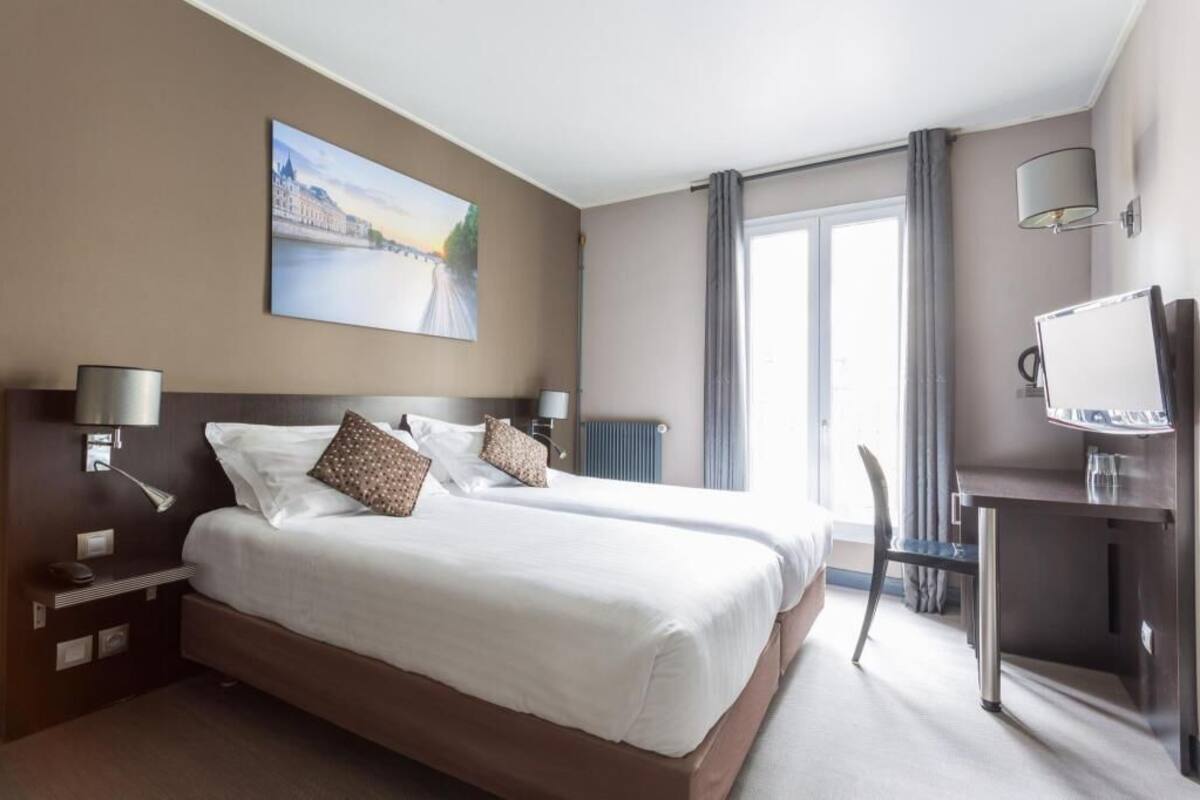 Une chambre d’hôtel avec deux lits, un bureau avec une chaise, une télévision et une grande fenêtre avec des rideaux.