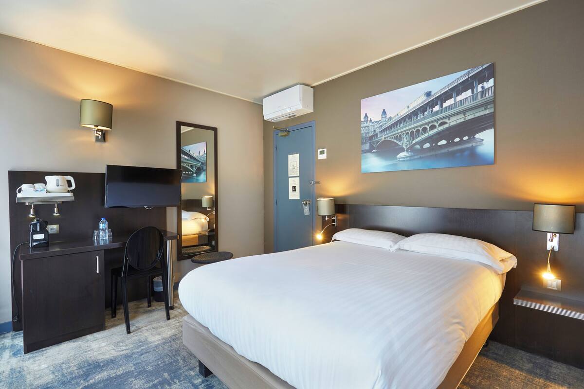 Une chambre d’hôtel avec un grand lit, un bureau avec une chaise, une télévision à écran plat, une machine à café et une bouteille d’eau.