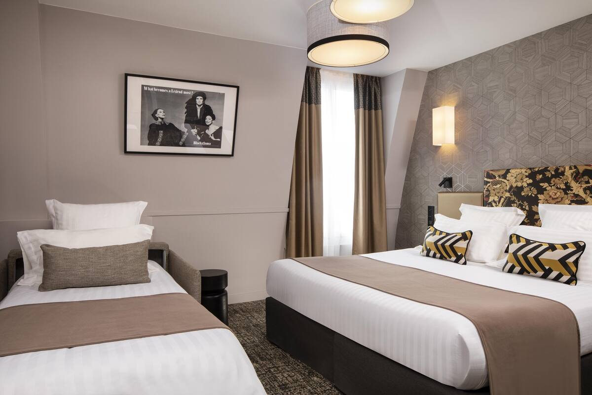 A hotel room with two beds, a framed picture on the wall, a lamp, and a patterned wall.