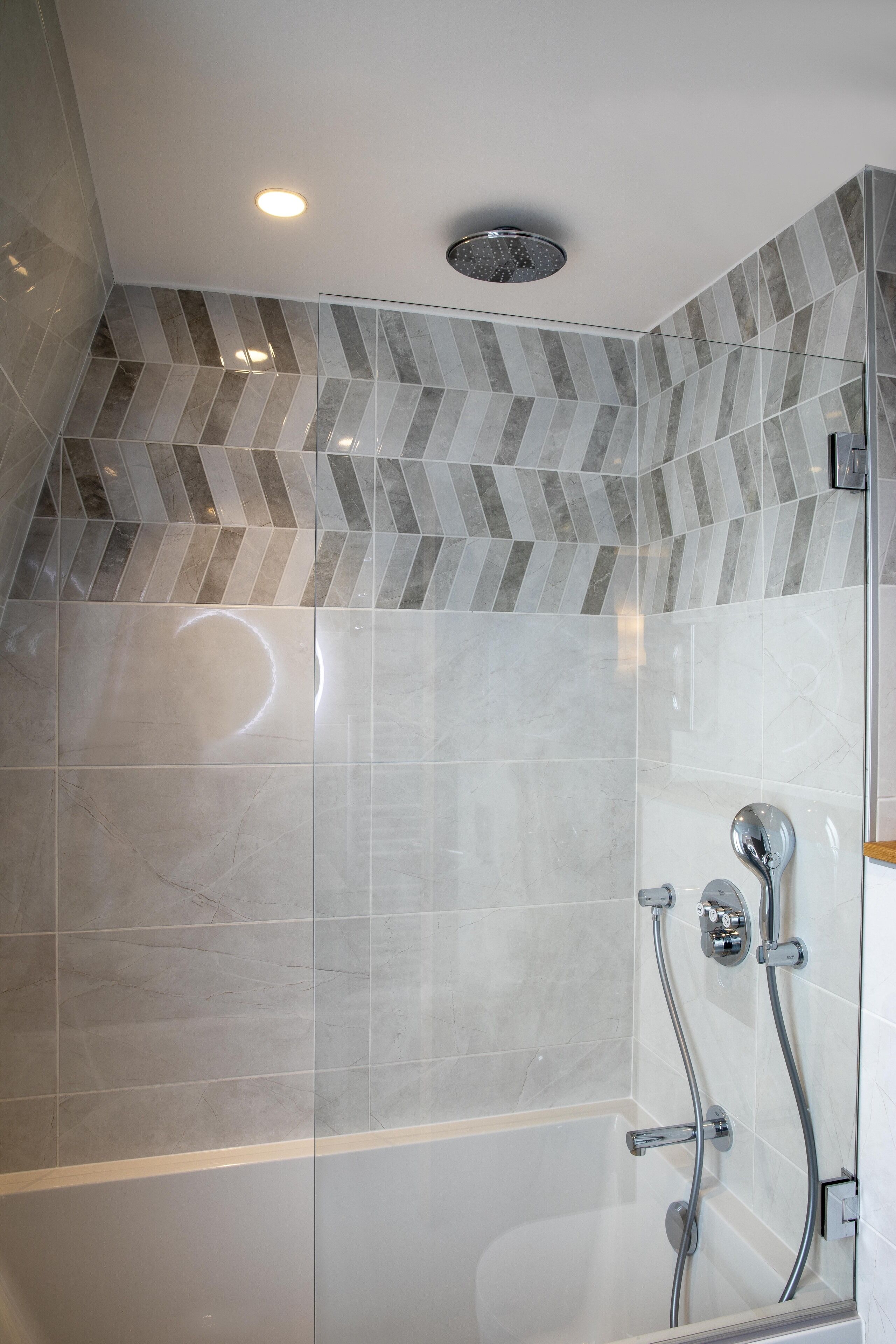 Um chuveiro moderno com porta de vidro, teto em padrão herringbone e chuveiro aparente.