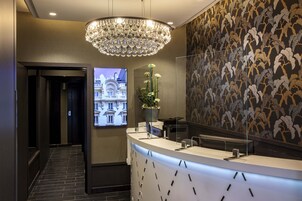 A modern hotel reception area with a large chandelier, a digital display of a building, and a patterned wall.