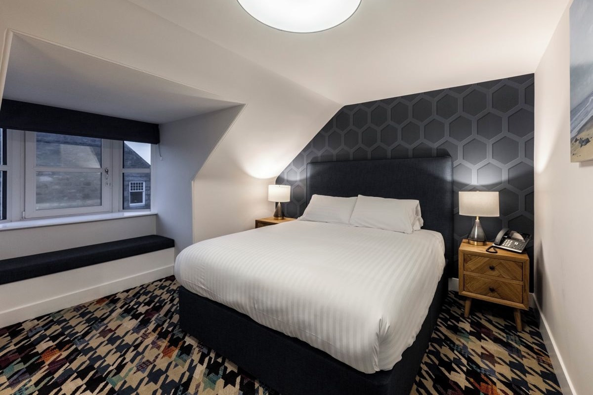 A bedroom with a large bed, bedside lamps, a window, and a patterned floor.