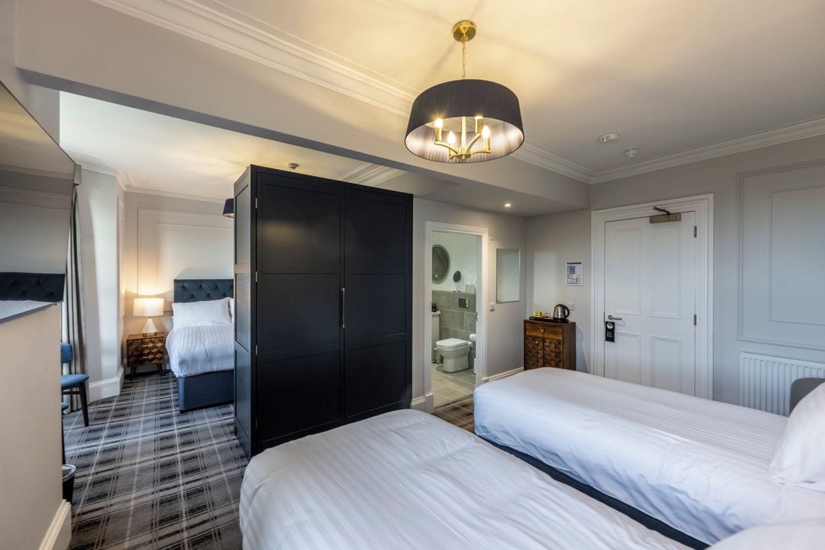A hotel room with a bed, a wardrobe, a desk, and a bathroom visible through an open door.