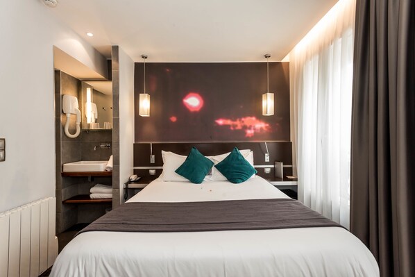 Una habitación de hotel moderna con una cama grande, un tocador integrado y un televisor de pared que muestra una luz roja.