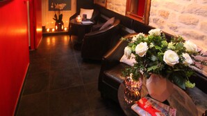 Un intérieur moderne avec un mur en pierre, un canapé en cuir, une petite table sur laquelle est posé un vase de fleurs, et un téléviseur sur le côté gauche.