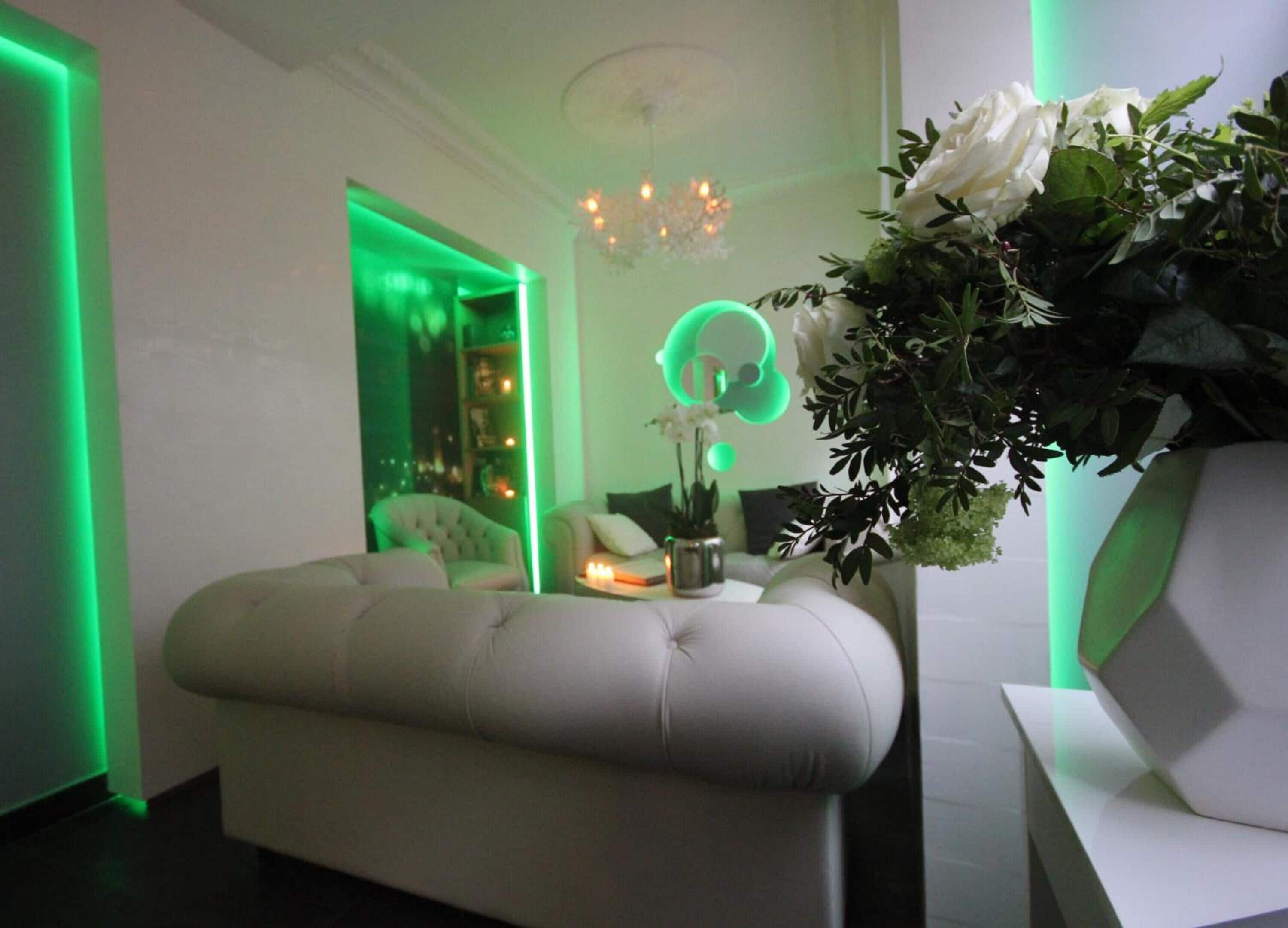 A modern room with a tufted bench, a green neon light, and a floral arrangement.