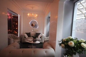 Una sala de estar moderna con sofá, sillones, una mesa de centro, una araña y un jarrón con flores.
