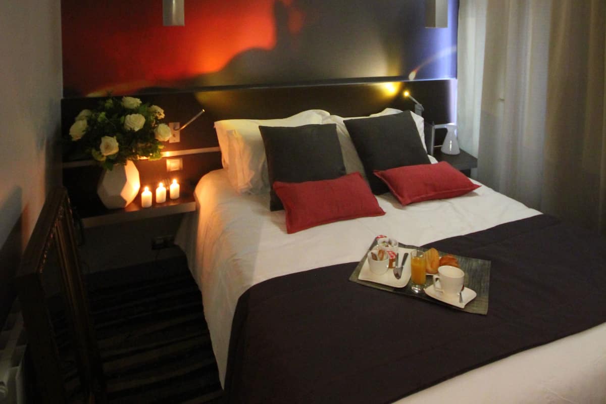 Habitación de hotel con cama, mesita de noche con velas, bandeja de desayuno y una pared con luz roja.