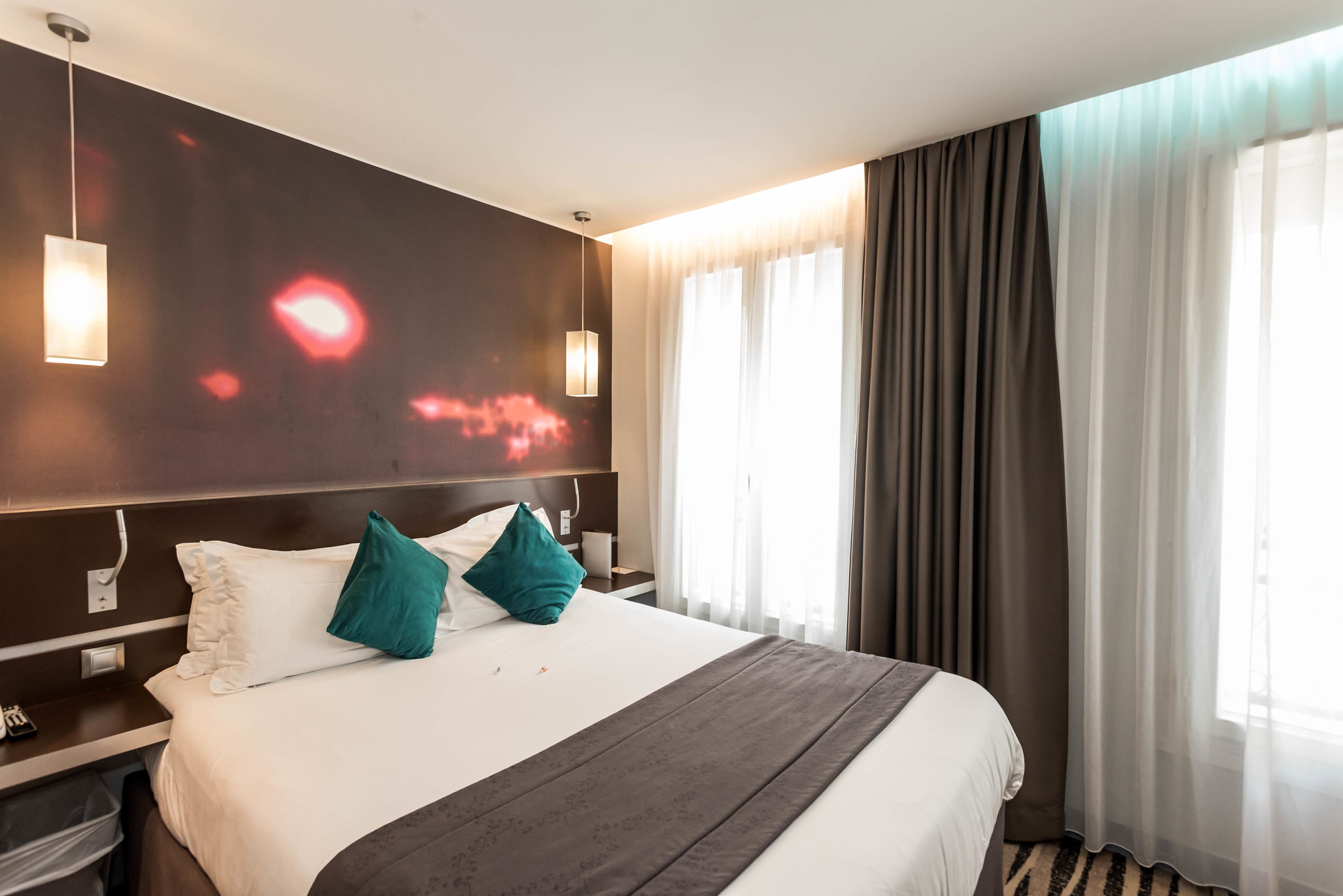 A hotel room with a large bed, two bedside tables, a wall-mounted TV, and a window with curtains.