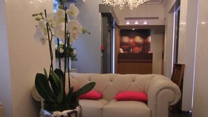 Un hall d’hôtel moderne avec un canapé beige, une orchidée en pot et une table ornée de bougies et d’un livre ouvert.
