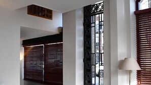 A hotel lobby with a reception desk, a floor lamp, a window with blinds, and a decorative metal gate. - Hôtel Moderne (Arras)