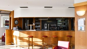 A bar area with wooden stools, a counter, and a clock on the wall. - Hôtel Moderne (Arras)