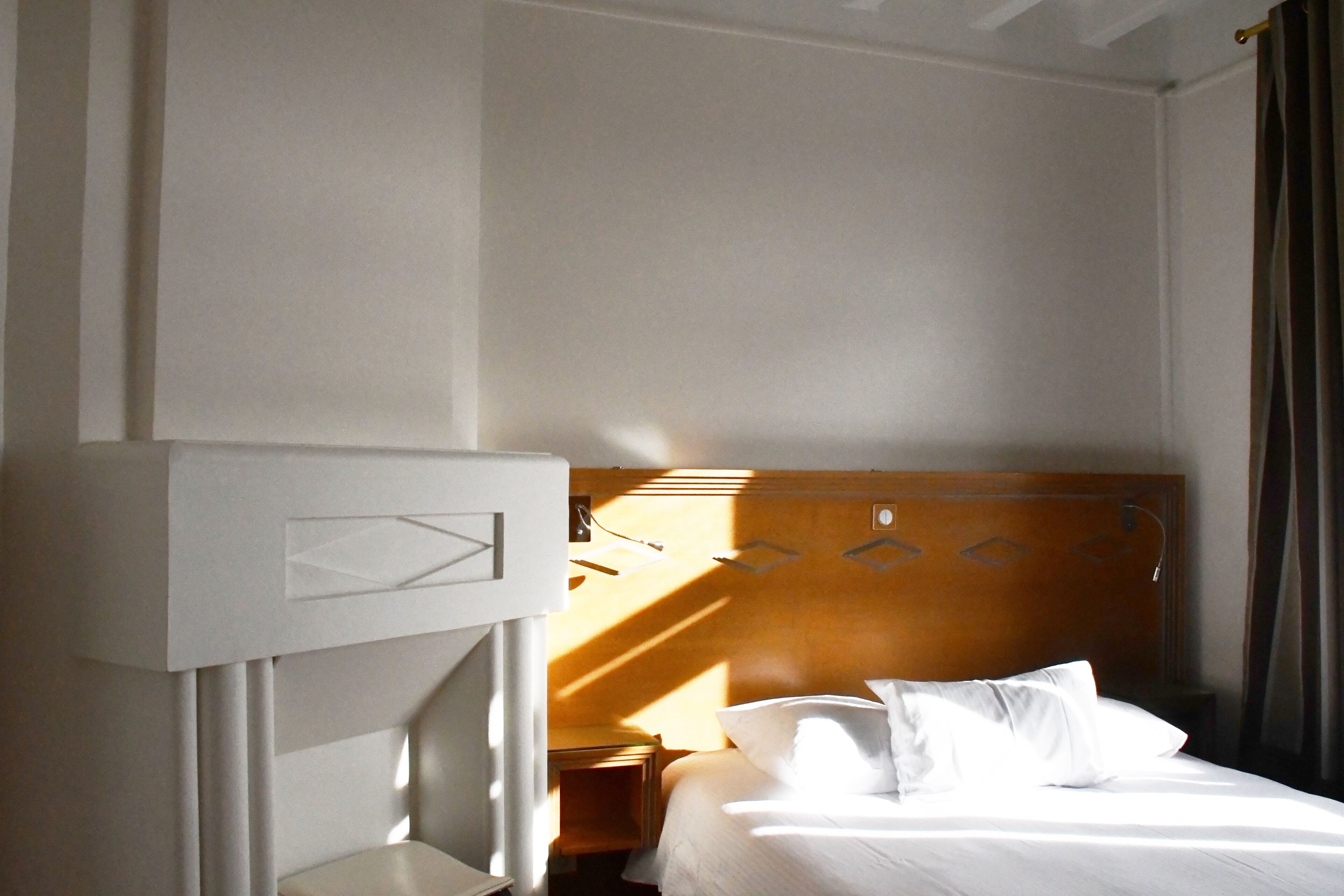 Une chambre d’hôtel avec un lit, une tête de lit en bois, une table de chevet et un bureau blanc.