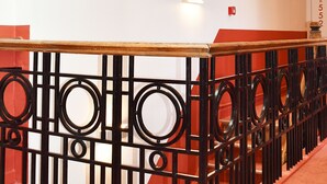 A staircase with a black metal railing featuring circular designs, a red carpet, and a white wall with a green emergency exit sign. - Hôtel Moderne (Arras)