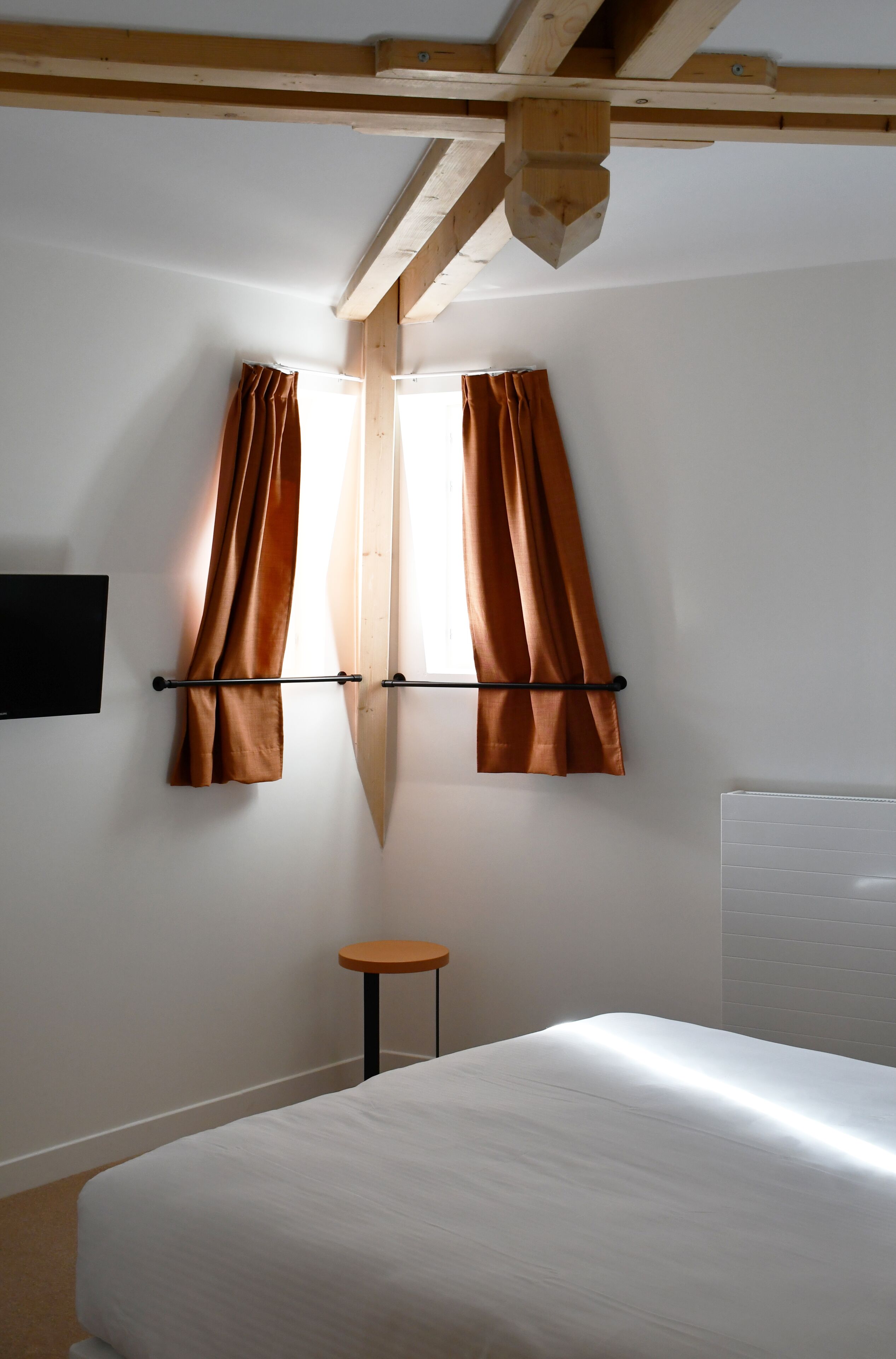 A bedroom with a bed, a small table, and two windows with curtains.