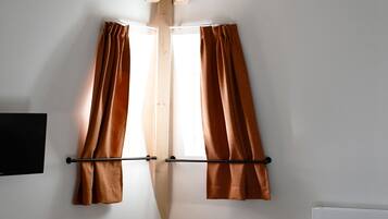 A bedroom with a bed, a small table, and two windows with curtains.