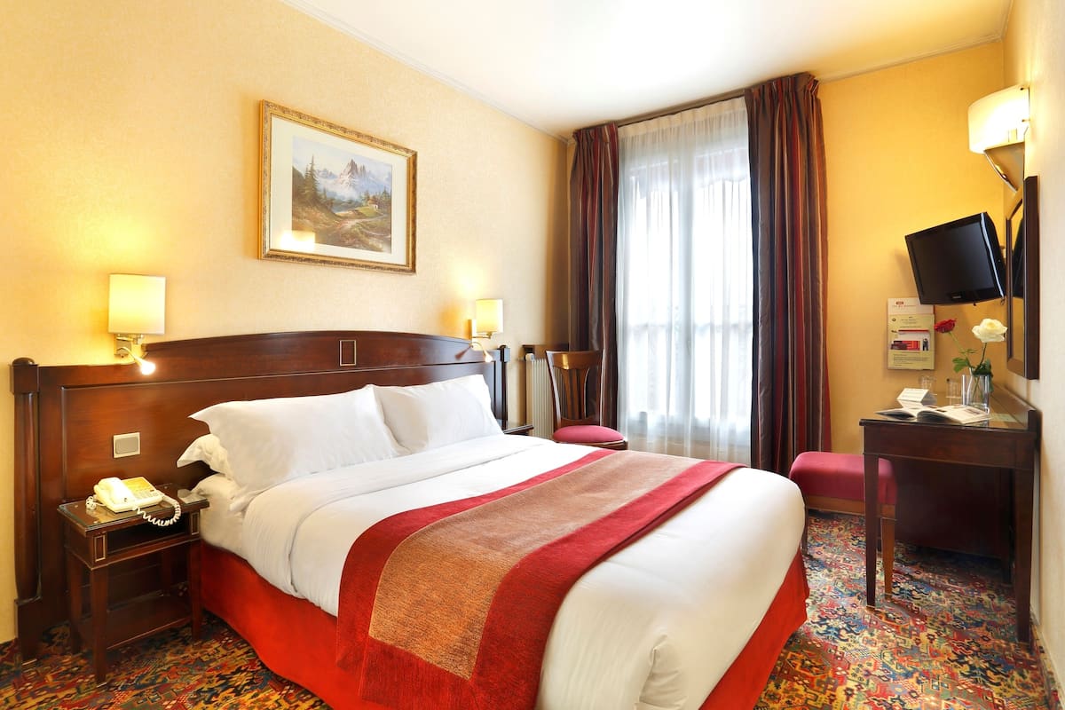 Een hotelkamer met een groot bed, twee nachtkastjes met lampen, een bureau met een computer en een schilderij aan de muur.