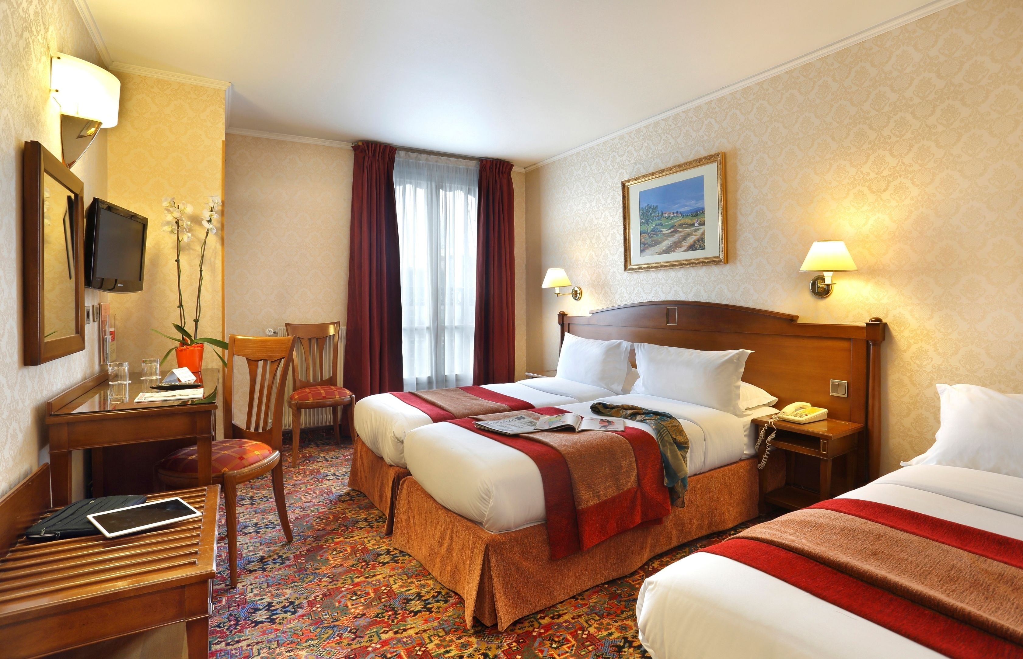 Une chambre d’hôtel avec deux lits, un bureau avec une chaise, une télévision et une fenêtre avec des rideaux.