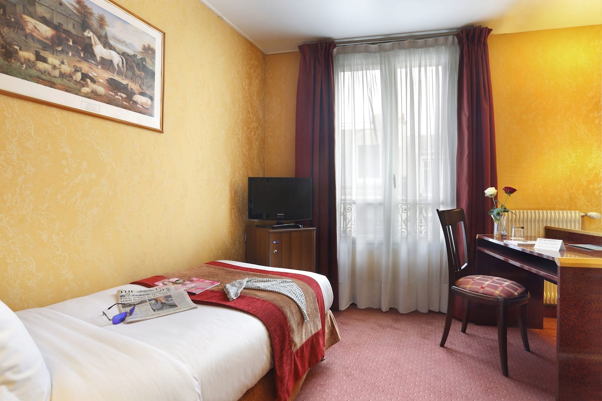 Een hotelkamer met een bed, een bureau met stoel, een televisie en een raam met gordijnen.
