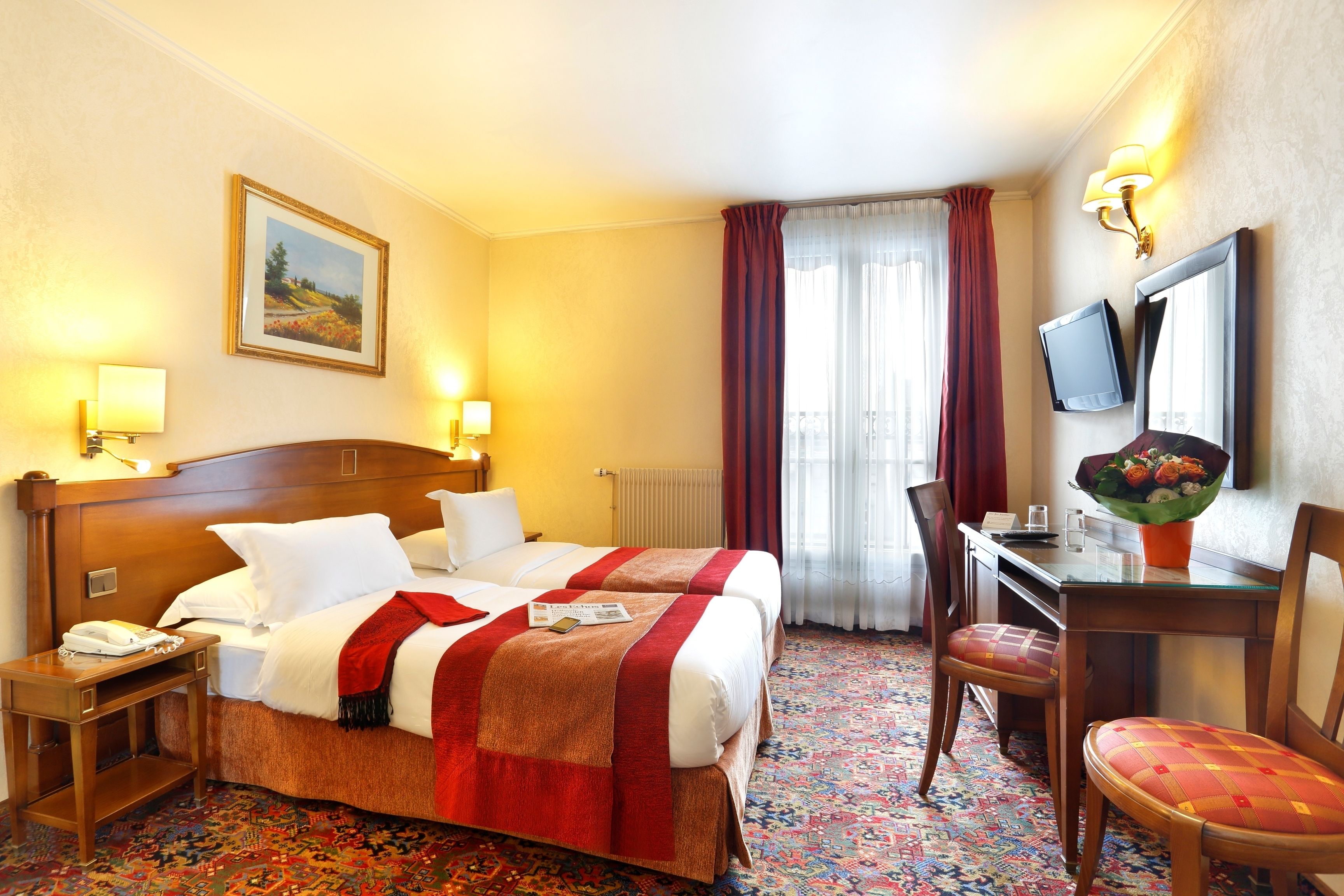 A hotel room with two beds, a desk with a chair, a TV, and a painting on the wall.