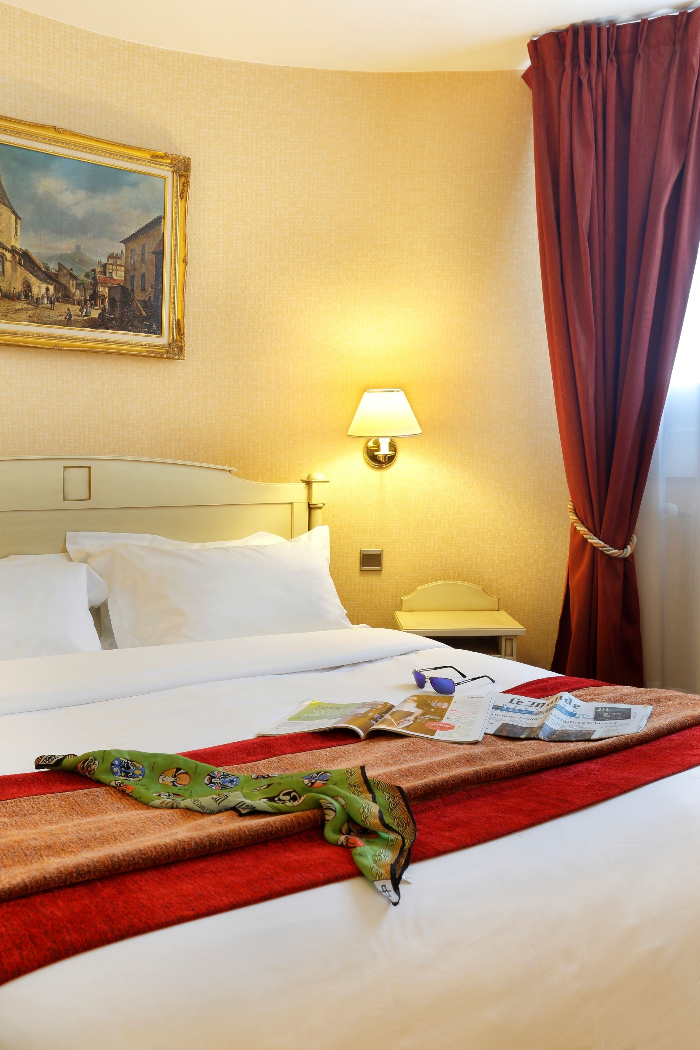 Une chambre d’hôtel avec un lit bien fait, une lampe, un tableau au mur et une fenêtre avec des rideaux.