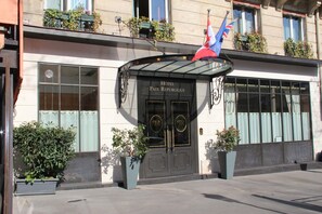Een hotelentree met een zwarte deur, een glazen luifel en een vlag.