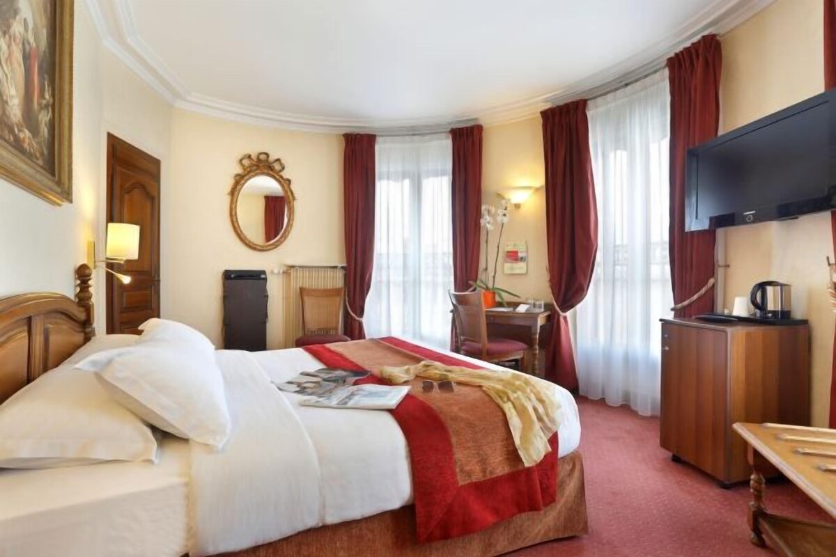 Une chambre d’hôtel avec un lit, un bureau, une chaise, une télévision et un tableau au mur.
