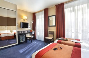 A hotel room with a bed, desk, chair, TV, and a view of the city through large windows.