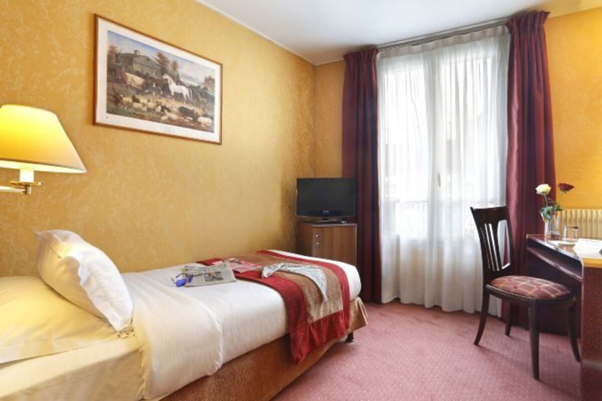 A hotel room with a bed, a desk, a chair, a television, and a painting on the wall.