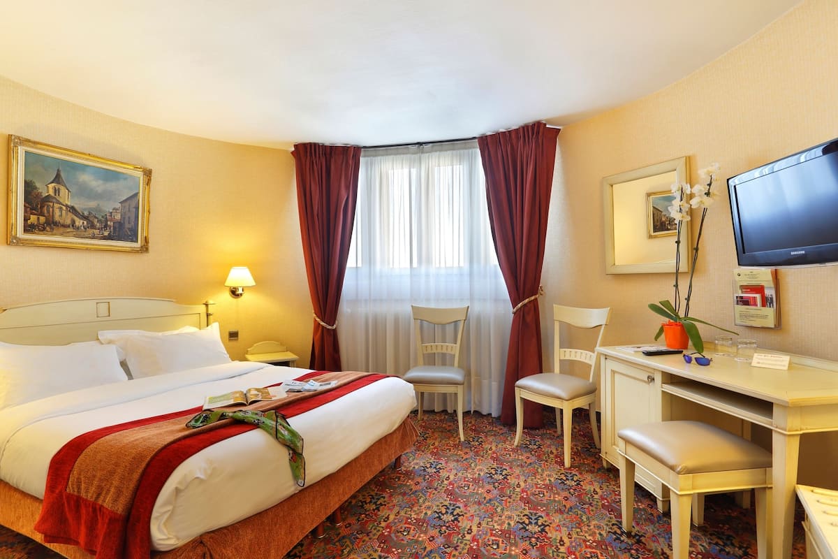 Een hotelkamer met een bed, een bureau, een stoel, een televisie en een raam met gordijnen.