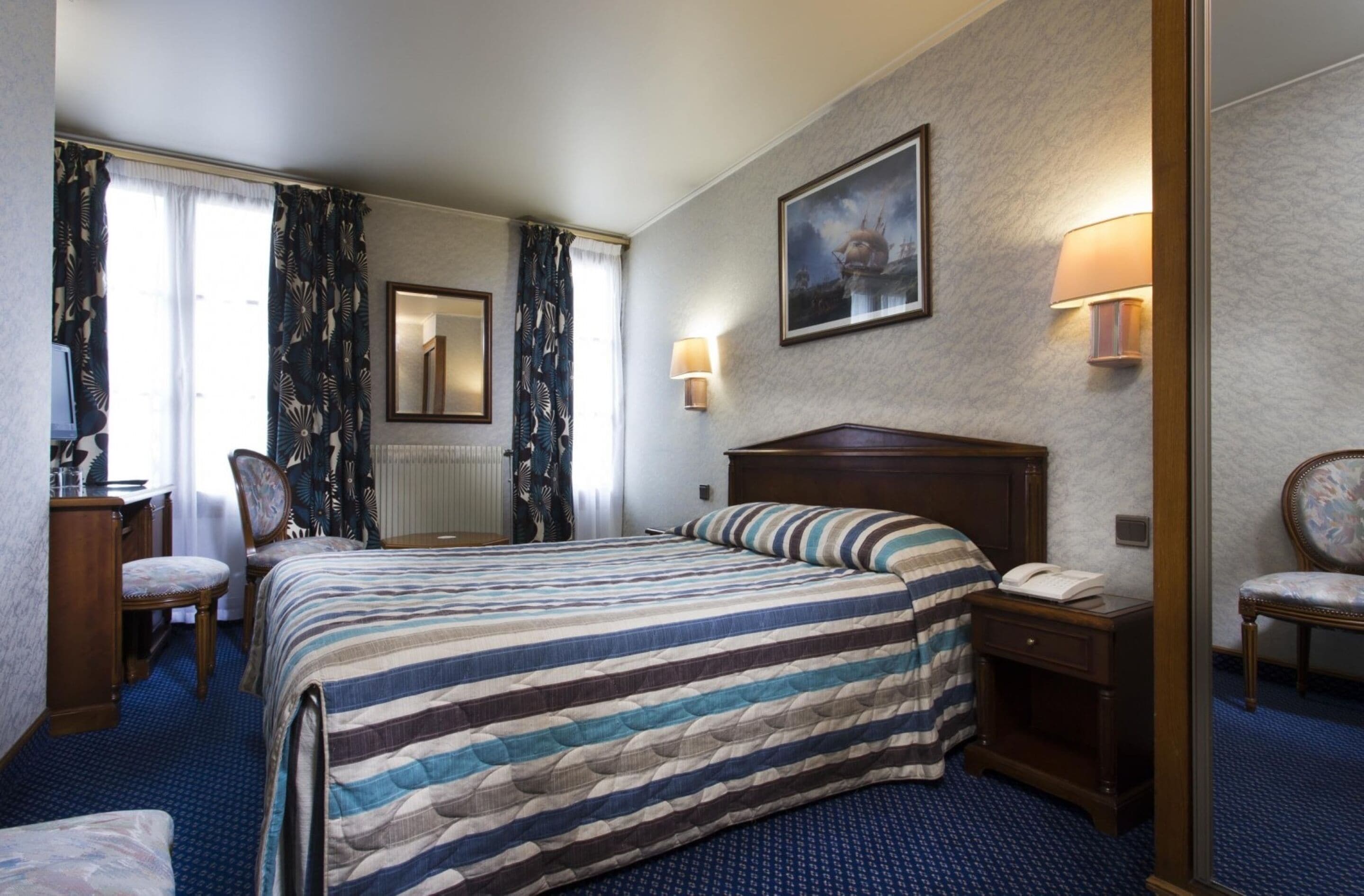 Une chambre d’hôtel avec un grand lit, un bureau avec une chaise, une lampe et un tableau au mur.
